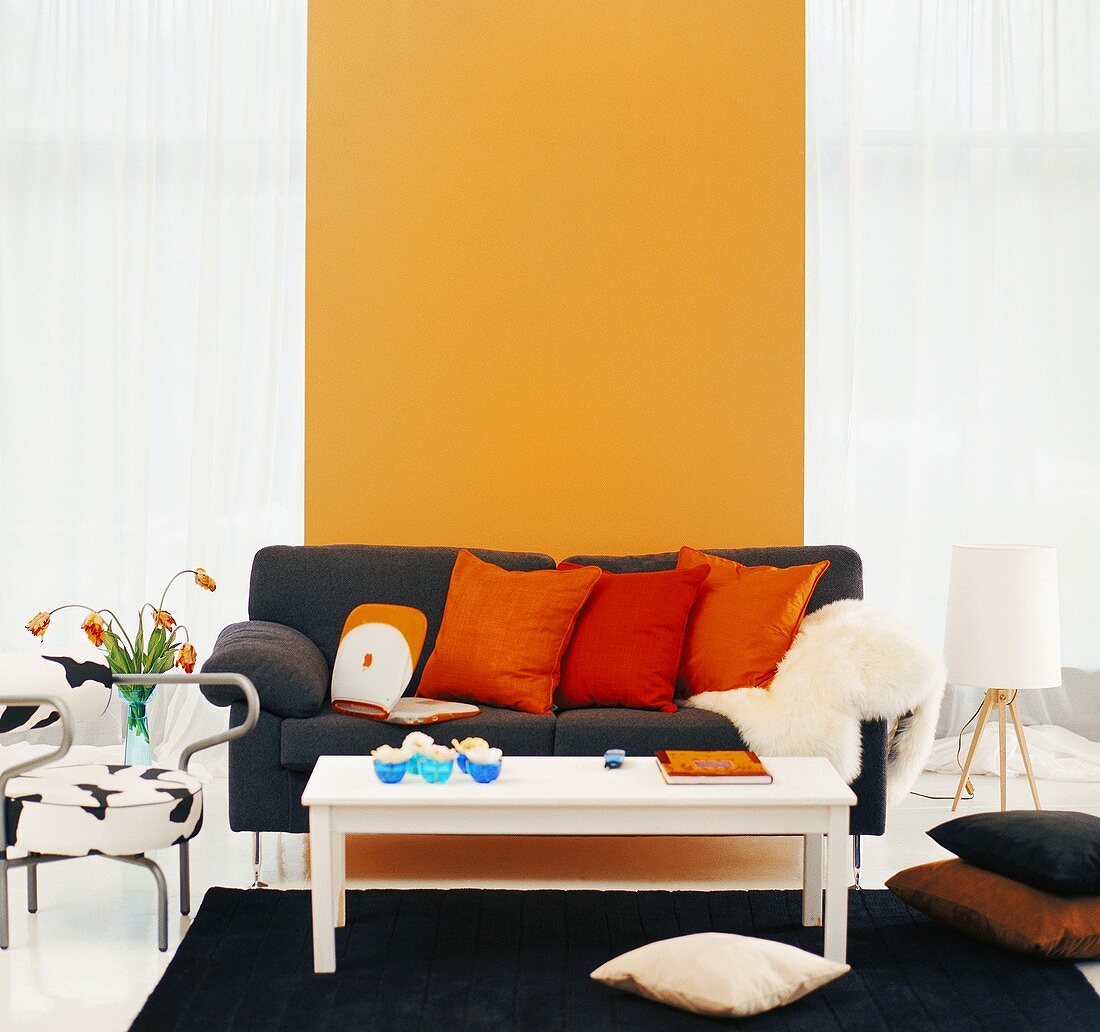 Schwarze Couch mit roten und orangen Zierkissen vor sonnengelber Wand