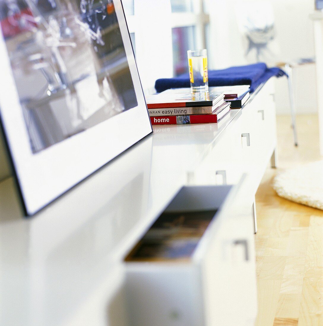 Reflektierendes, weißes Sideboard mit Bild und Bücherstapeln im Wohnzimmer