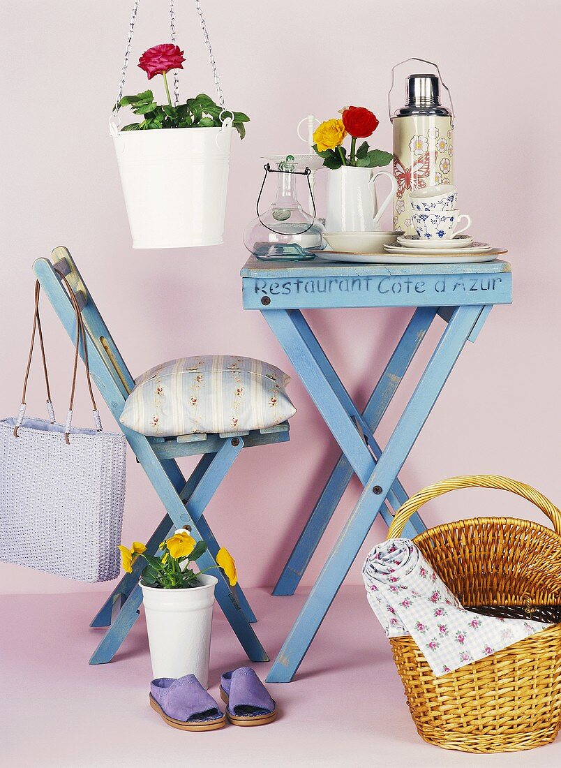 Blauer Tisch mit Geschirr, Stuhl, Korb und Blumen