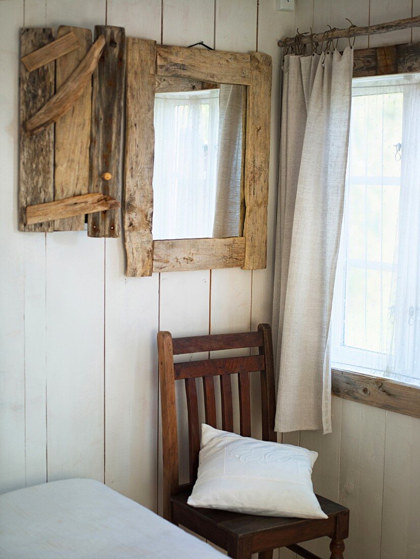 Einfaches Schlafzimmer mit weiß lackierten Holzwänden und einem Spiegel mit rustikalem Holzrahmen