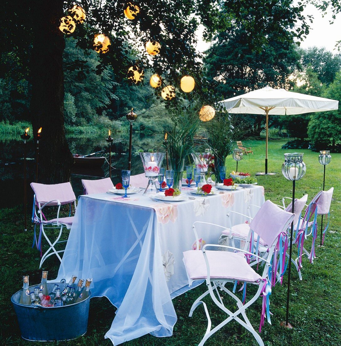 Festlich gedeckter Tisch im Garten mit Blumen, Windlichtern, Lampionkette & Gartenfackeln