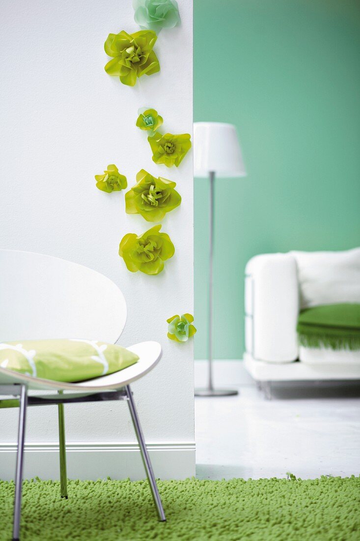 Weisser Stuhl mit Kissen vor weisser Wand mit grünen Papierblüten, daneben Spiegel