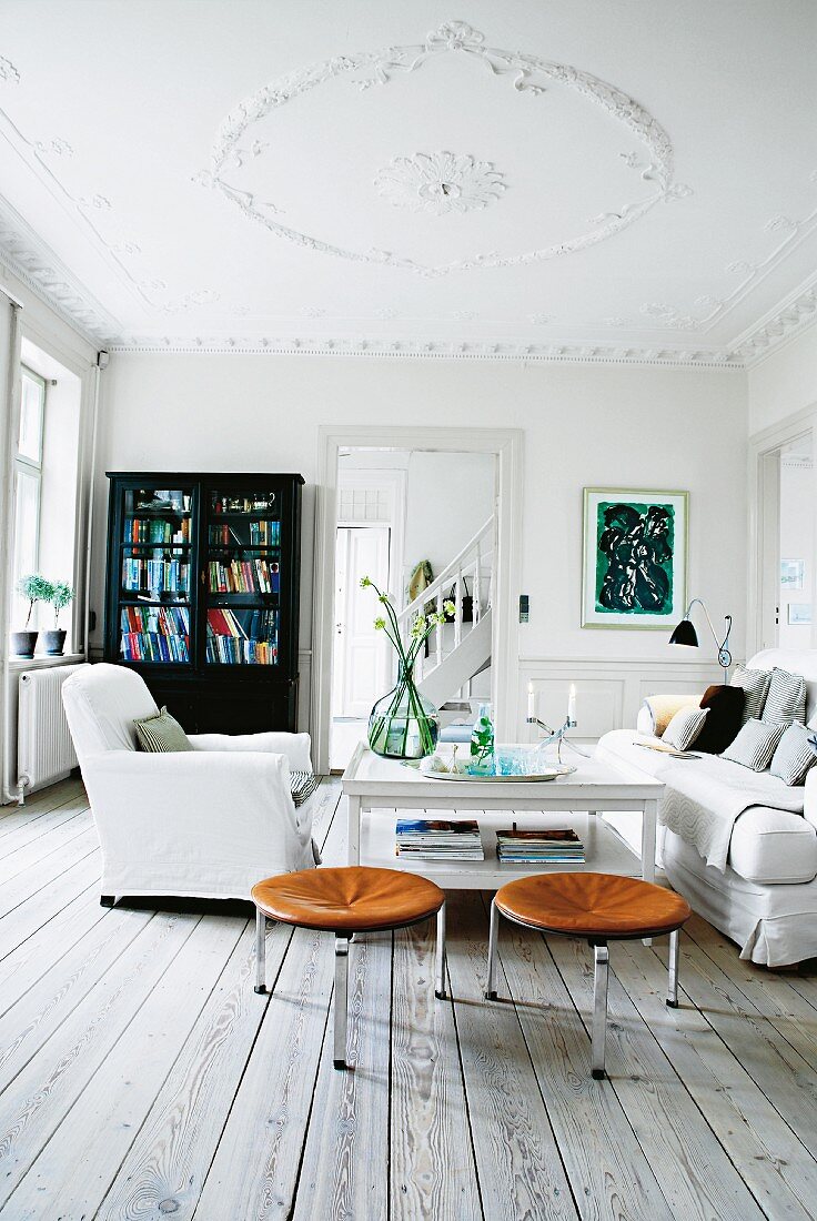 Weisses Wohnzimmer mit schwarzem Schrank, Hussensessel und Lederhocker