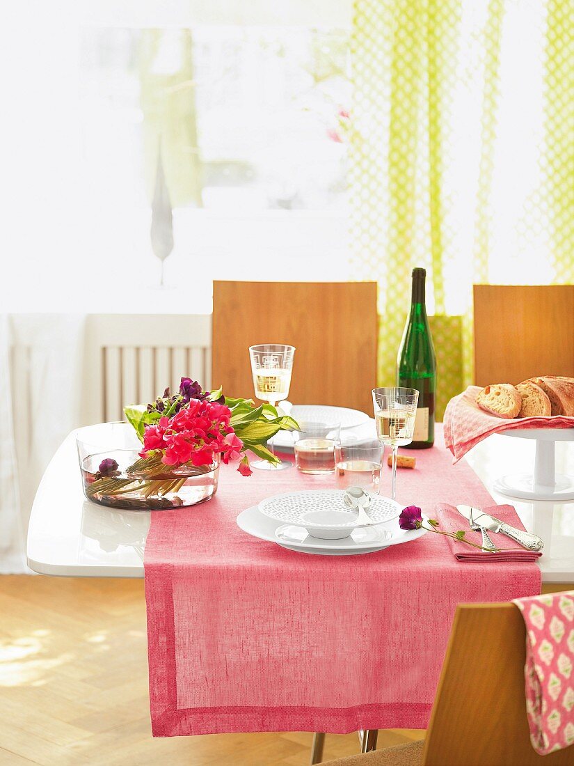 Gedeckter Tisch mit rosafarbenem Tischläufer & Blumenschale in lichtdurchfluteten Esszimmer
