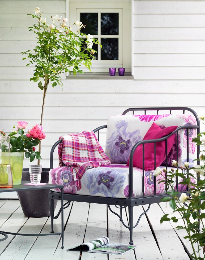 Armlehnstuhl aus Metall mit Kissenauflagen im Blütendesign auf sommerlicher Veranda
