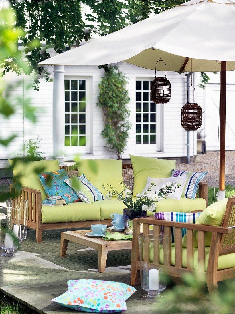 Gartenmöbelsitzgruppe aus Holz mit grünen Posterauflagen unter Sonnenschirm auf Terrasse