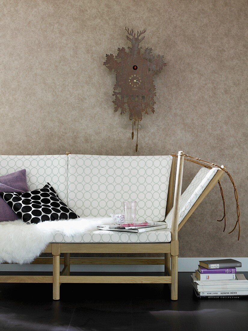 Sofa mit Holzgestell im Retro-Look, darüber Kuckucksuhr an der Wand