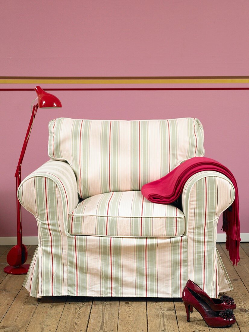 Sessel mit gestreiftem Bezug und rote Metall-Stehleuchte im Retrostil vor rosa Wand