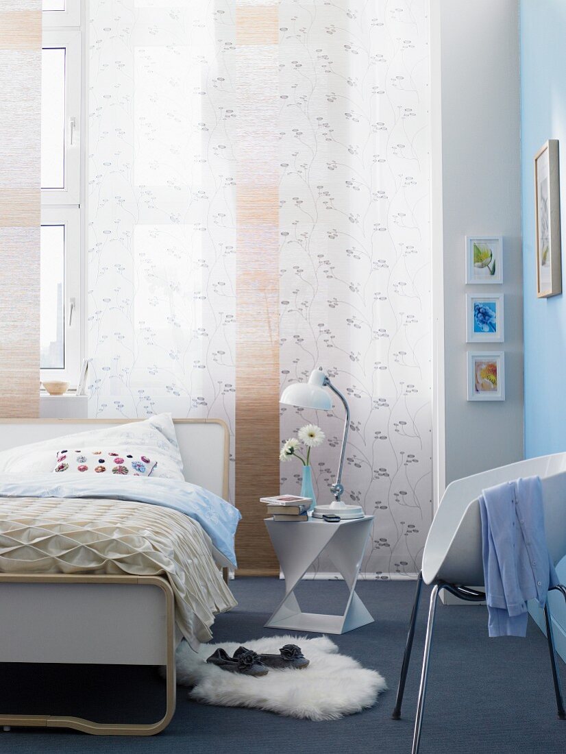 Bed below windows with panel curtains in bedroom with pale blue wall