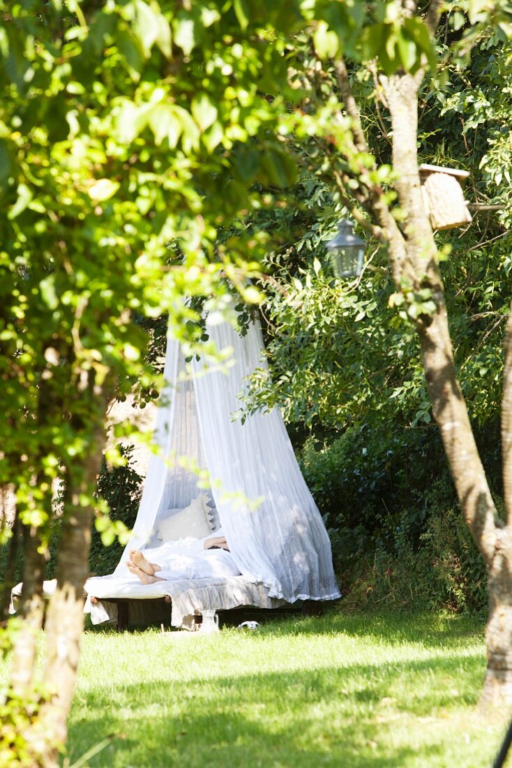 A person relaxing under a white canopy in a garden