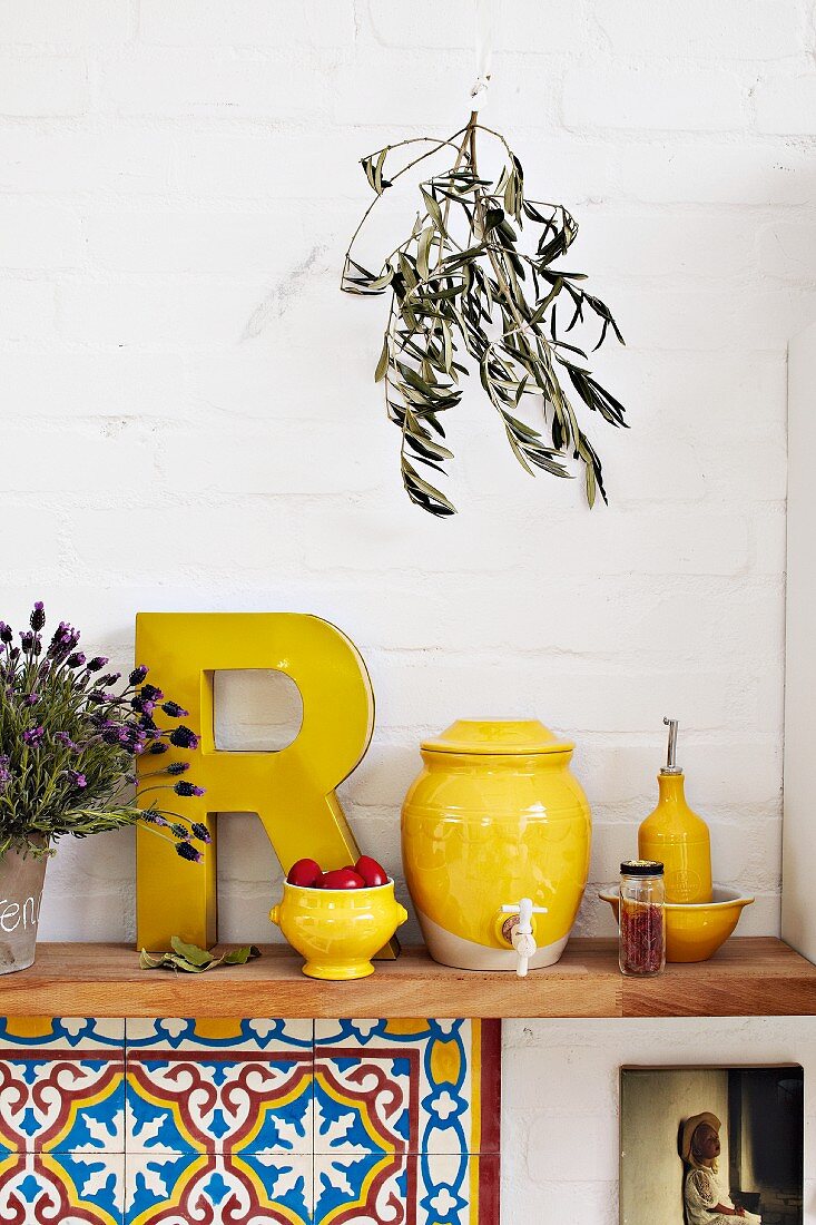 Yellow kitchen utensils such as vinegar pot and oil bottle on wooden shelf in Mediterranean kitchen