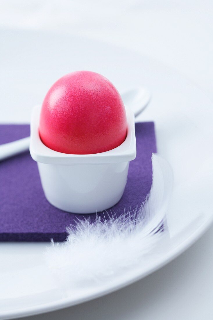 Gefärbtes Ei in schlichtem Eierbecher auf violettem Filzuntersetzer