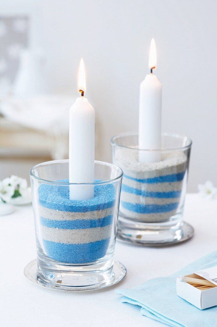 weiße, brennende Kerzen in Glas mit hellem und blauem Sand