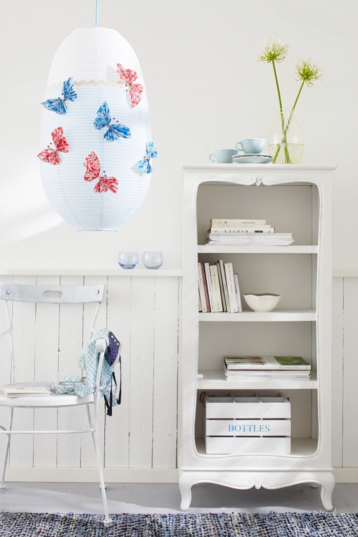 A living room in white with a chair, a shelf and a paper lamp decorated with butterflies