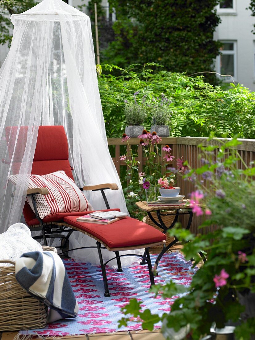 Balkon mit rotem Deckchair, Moskitonetz, Beistelltisch und Blumen