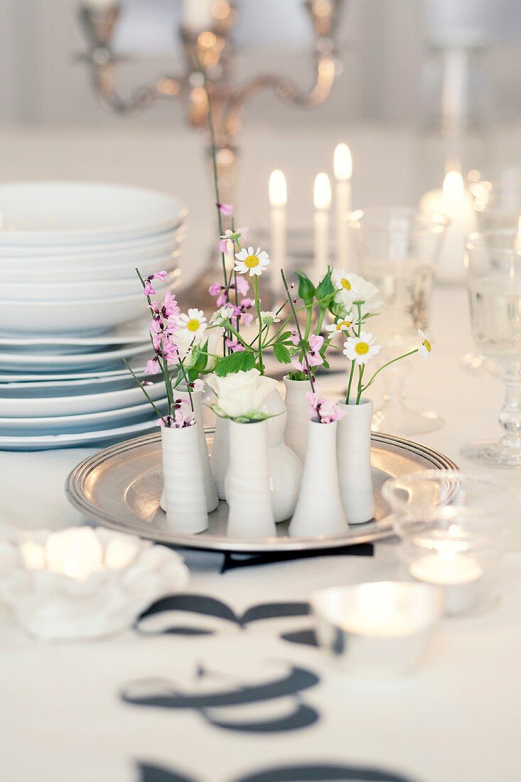 Blumen in kleinen Vasen auf Tablett als festliche Tischdekoration