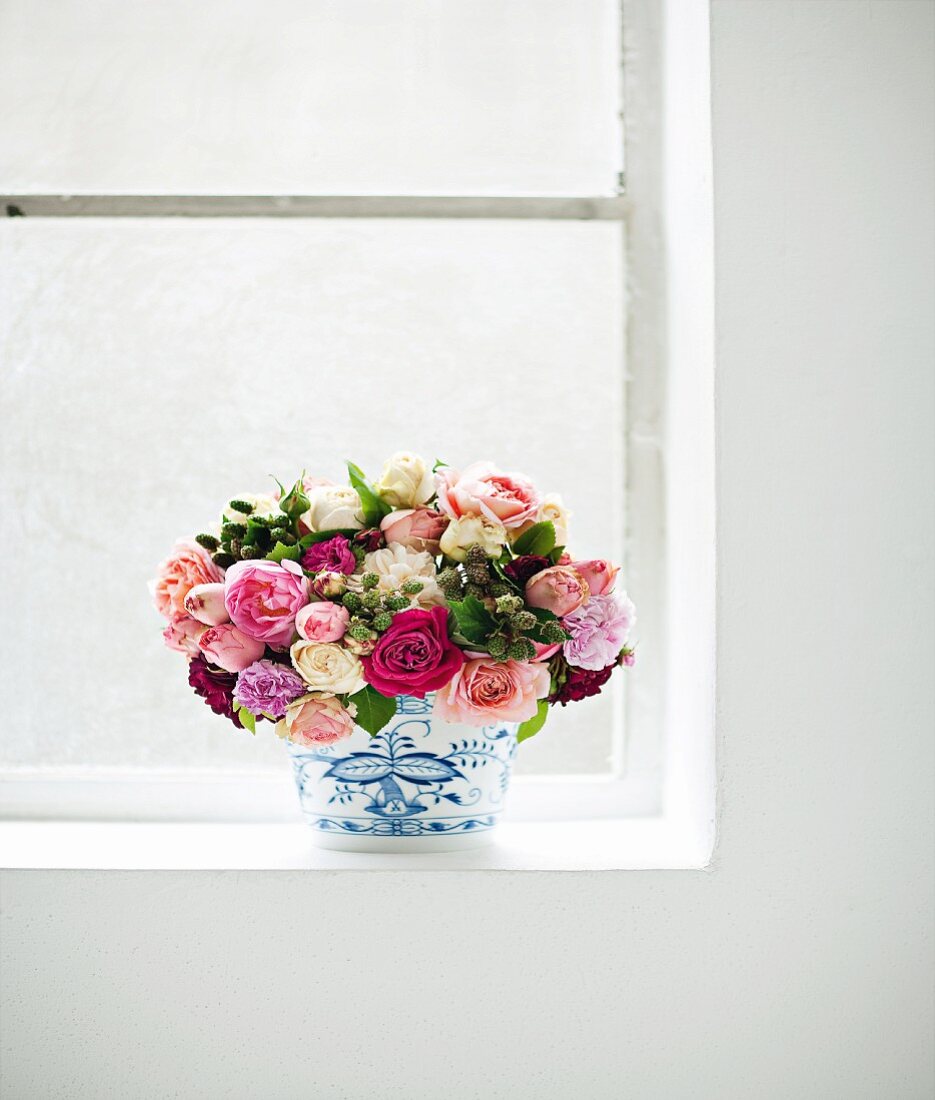 Blumenstrauß aus Freilandrosen in einer Vase am Fenster