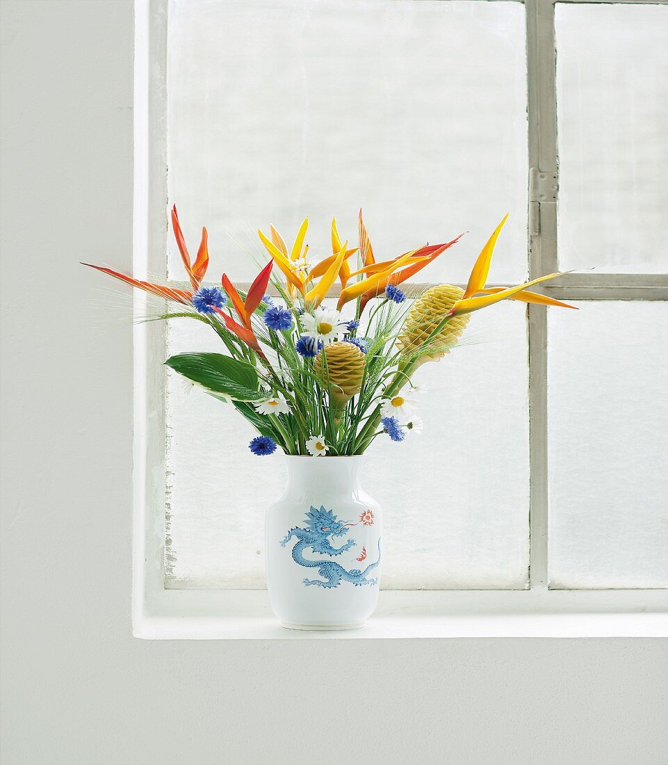 Strauss aus langstieligen Blumen - Helikonien und Ingwerblüten - in einer Vase am Fenster
