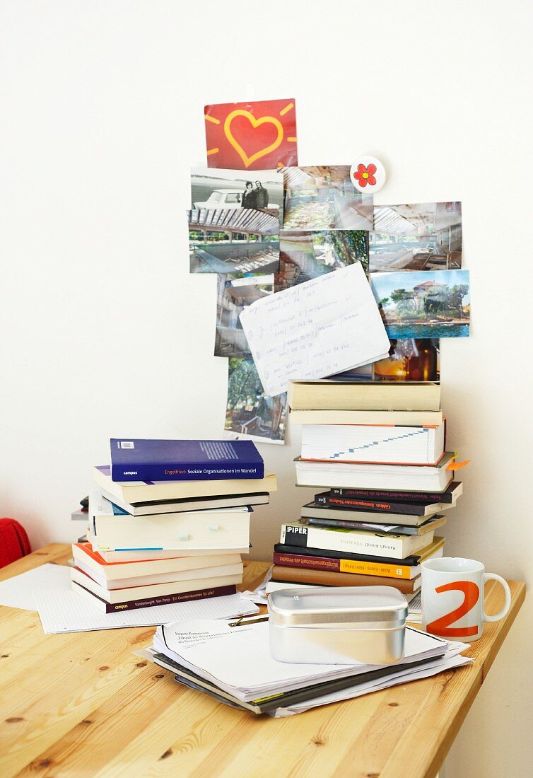 Gestapelte Bücher & Postkarten an Wand einer Studentenwohnung