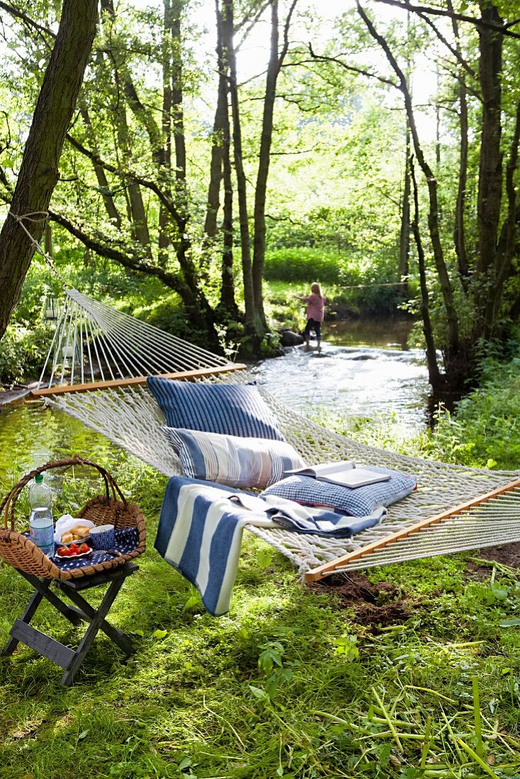 Hängematte mit Kissen und Hocker mit Picknickkorb im Wald