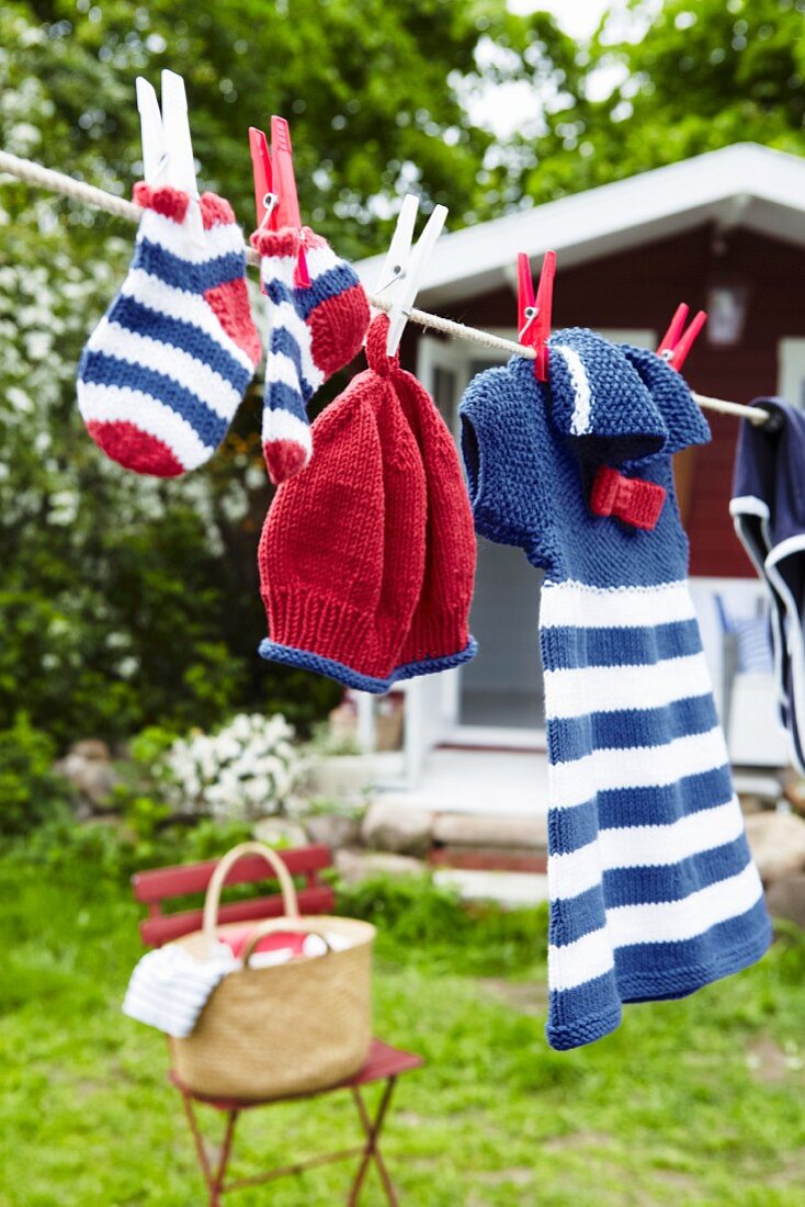 Knitted baby clothes hanging on a washing line in a garden