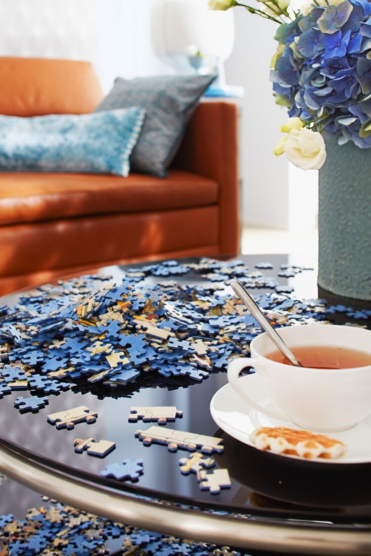 Couchtisch mit Puzzleteilen und einer Tasse Tee, im Hintergrund Ledercouch