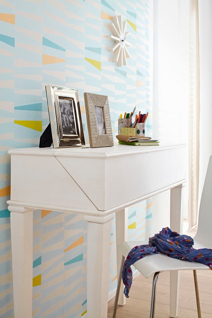A white bureau against a wall with geometric patterned wallpaper