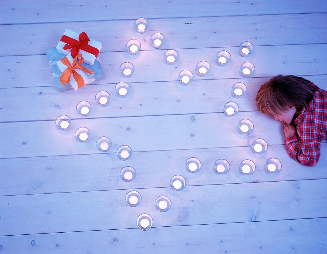 Kind liegt auf Dielenboden neben Stern aus Teelichtern & Geschenkpäckchen