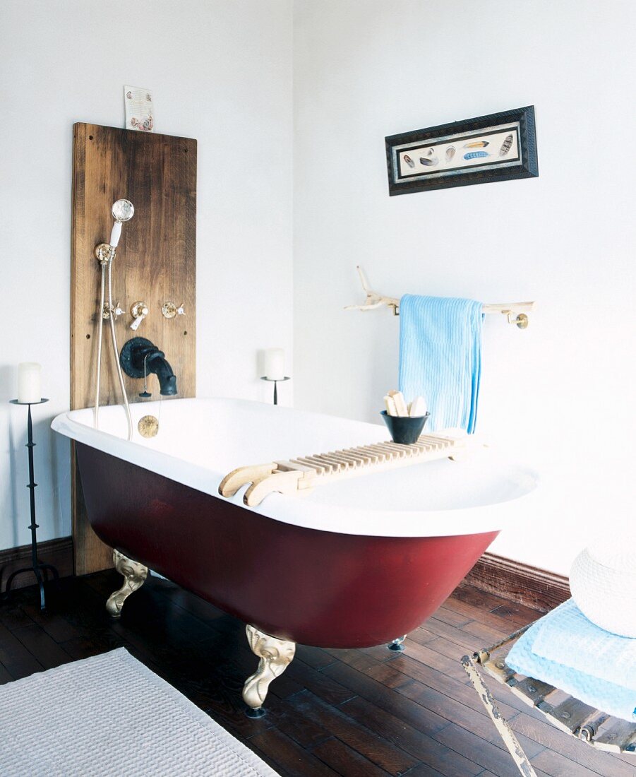 Freistehende Vintage Badewanne mit Ablage vor Holzpaneel an Wand mit Duscharmatur in schlichtem Badezimmer