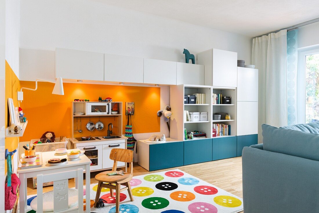 Spielecke im Wohnzimmer - mit Miniküche zwischen Schrankelementen und Kindertisch auf Teppich mit buntem Knopfmuster