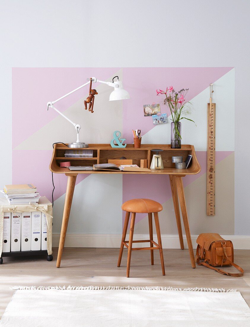 A delicate home office desk made from curved, laminated wood and a ringbinder trolley with the wall painted with pastel-coloured triangles