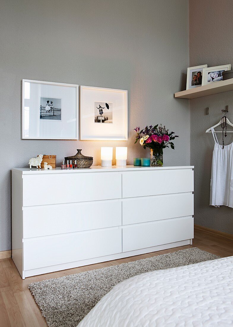 Framed photos over a white chest of drawers in a bedroom with grey walls