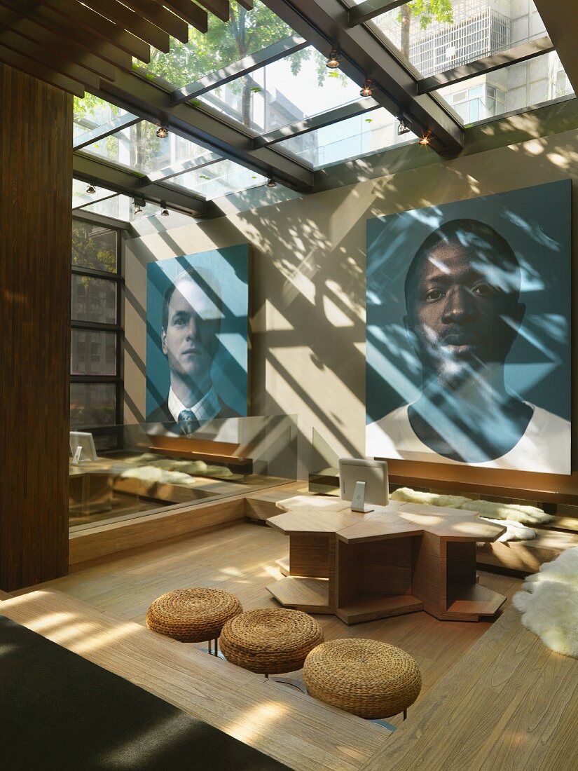 Moderner Arbeitsplatz mit Glasdach und schlichte Holzmöbel vor grossformatigen Portraits an Wand