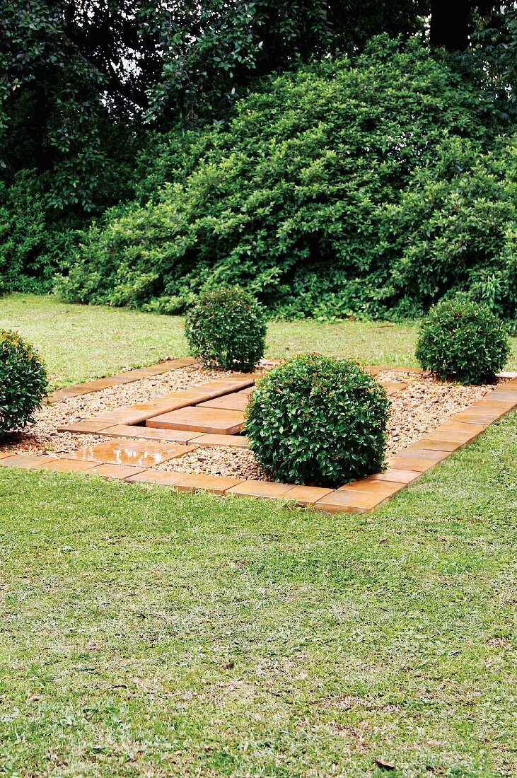Angelegter Wasserlauf mit Steinplatten und Kies, runde Buxbäumchen begrenzen die geometrische Gartenarchitektur