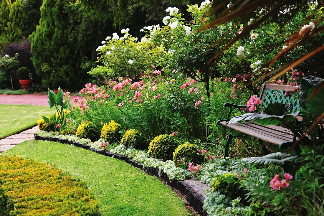 Schattenplatz mit Gartenbank in prächtig blühendem Garten mit gepflegtem Rasen