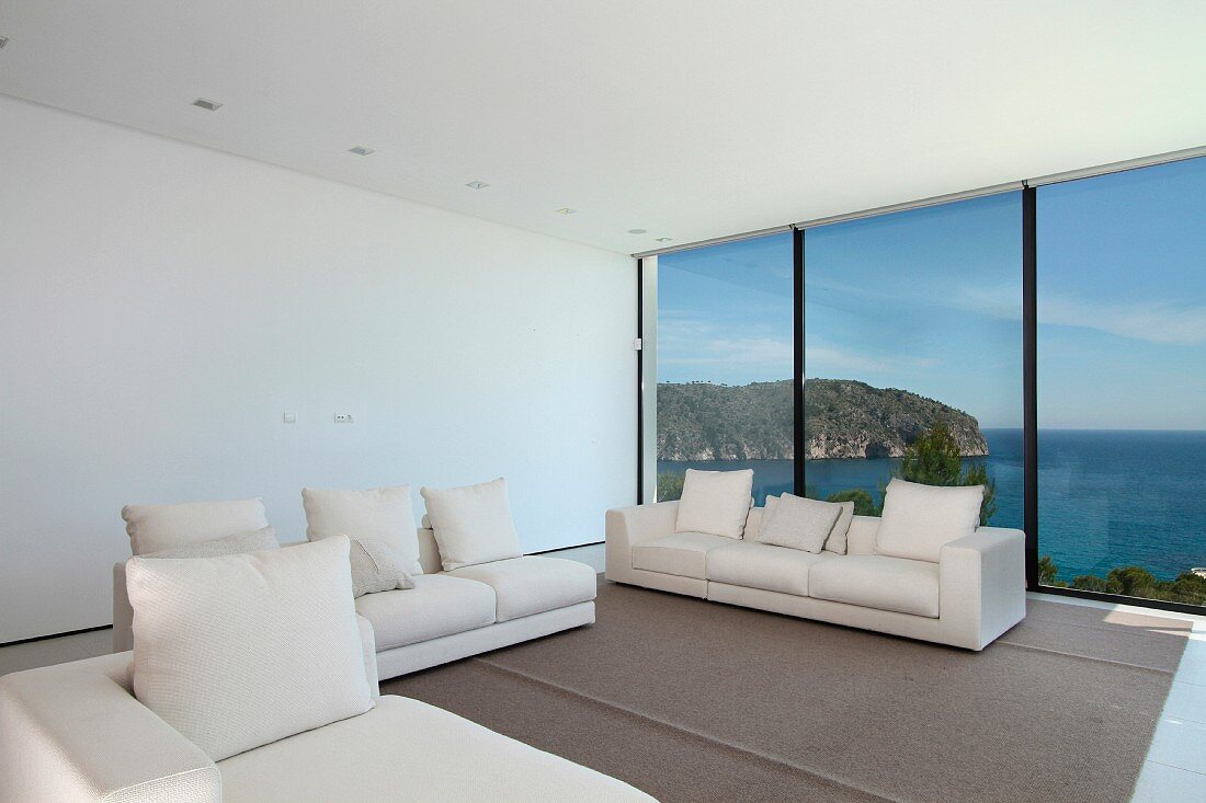 Helle Sofagarnitur im minimalistischen Wohnraum mit Fensterfront und Meerblick