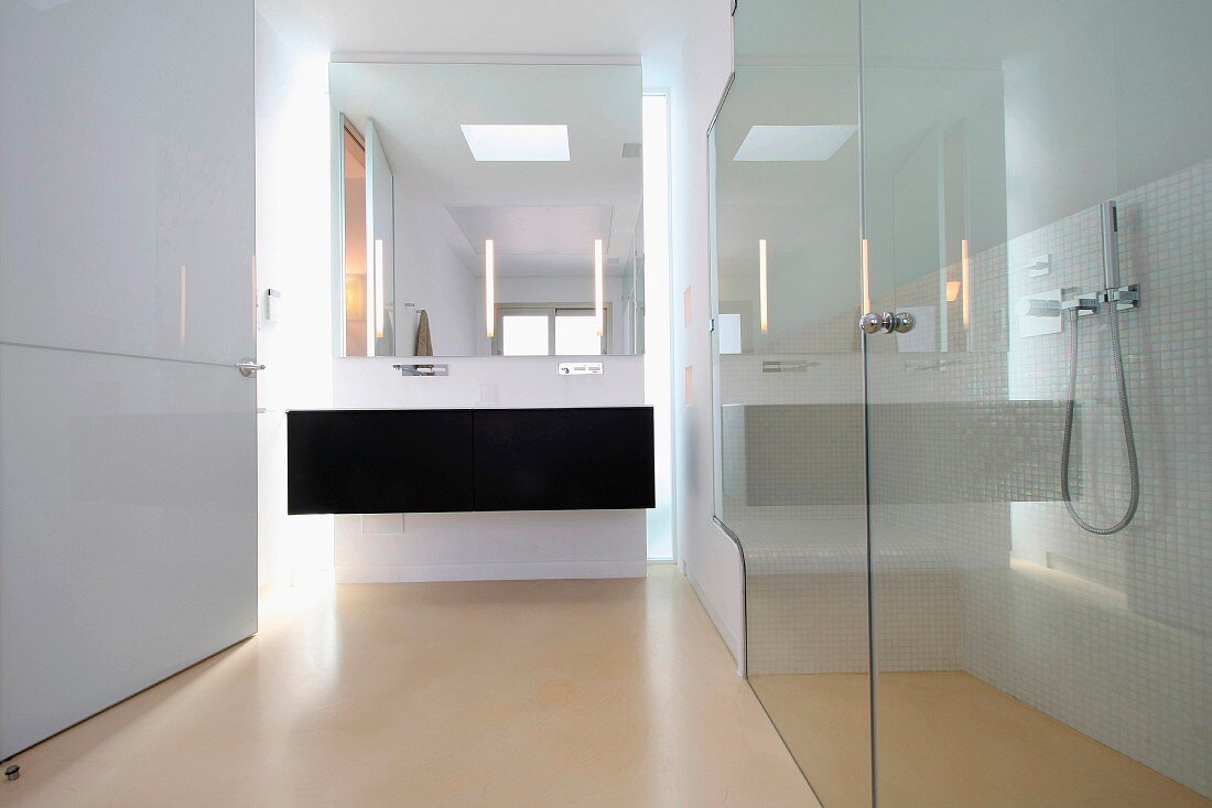 Verglaster Duschbereich und schwarzer Waschtisch in weißem Designerbad