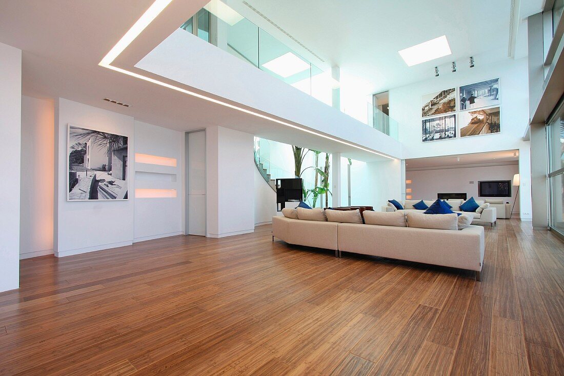 Offener Designer Wohnraum mit heller Polstergarnitur auf Holzfussboden und Blick auf Galerie