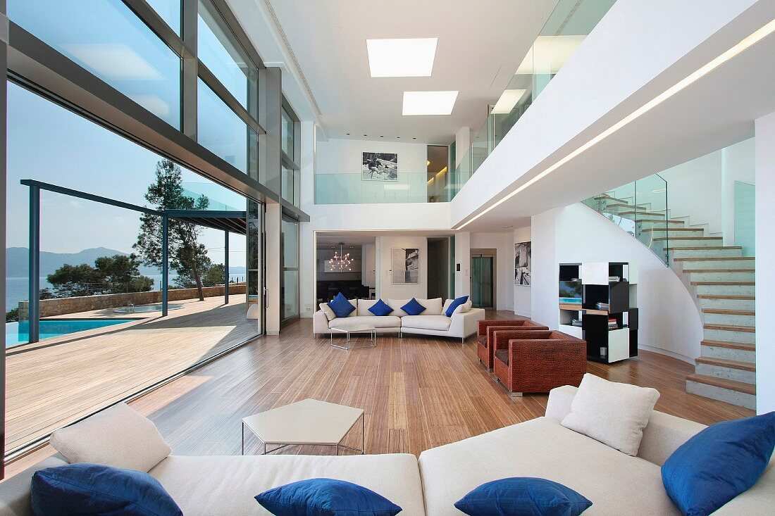 Designer Wohnraum mit geschwungenem Treppenaufgang und offener Glasfront vor Terrasse