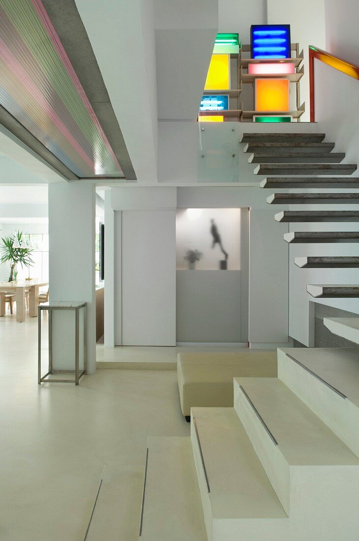 Farbige Leuchtobjekte am oberen Absatz einer modernen Treppe im weissen, offenen Wohnraum