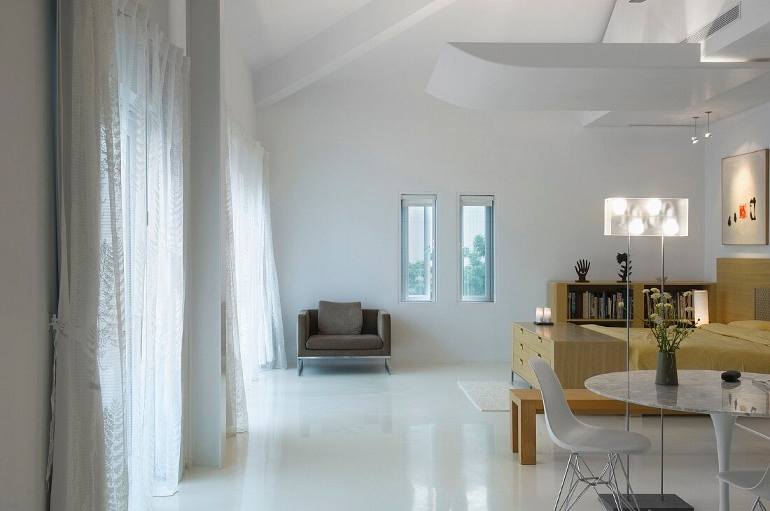 Offener Wohnraum mit spiegelnd weißem Boden und indirekter Beleuchtung gegen das geneigte Dach