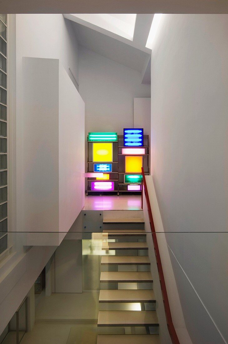 Blick durch Glasbrüstung auf aus der Wand auskragende Treppenstufen und Regal mit bunten Leuchtkästen in Designerwohnung