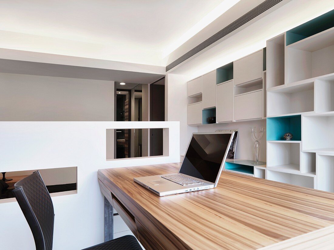 Helles, modernes Home Office mit Laptop auf Holztisch und weißem Regalsystem