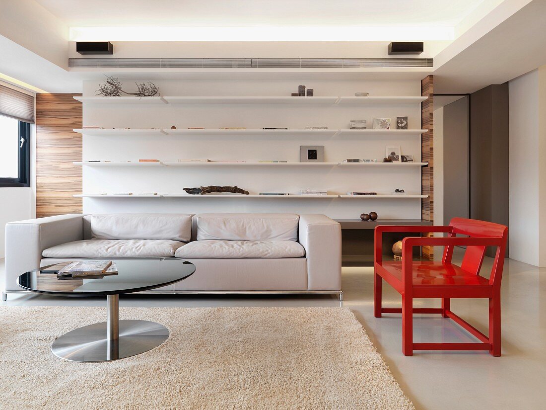 Graues Sofa und roter Armlehnstuhl aus Holz vor Designer Einbauregal