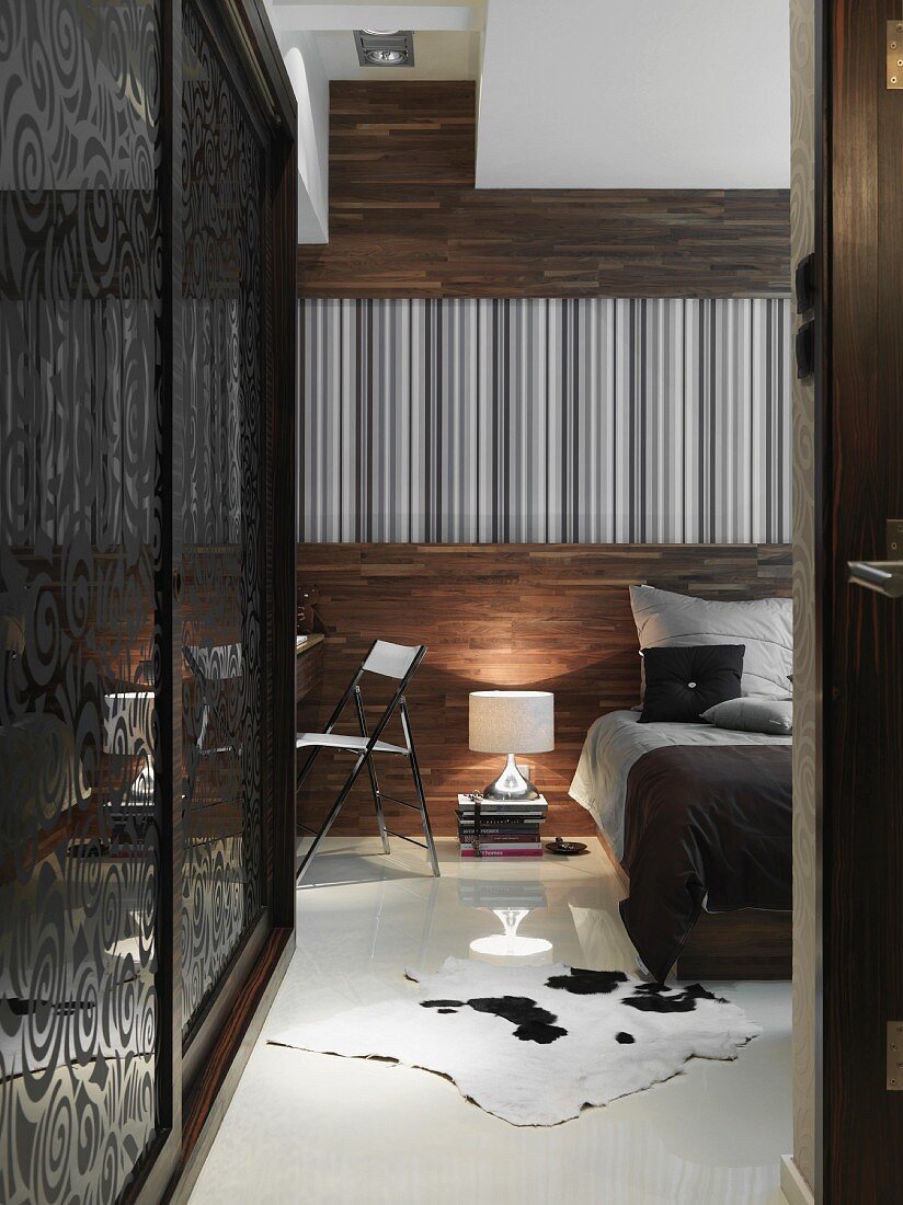 Bed with grey and black covers in front of wood-panelled wall and fitted wardrobe to one side with sliding doors