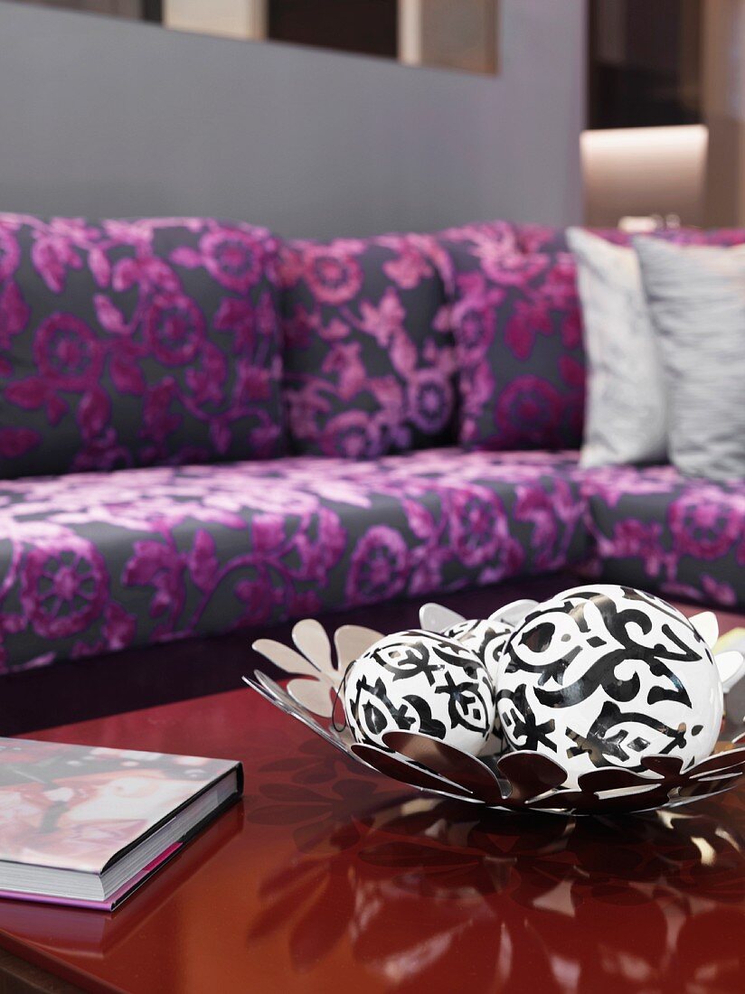 White spheres with black patterns in bowl with flower motif and purple patterned, classic modern sofa in blurred background