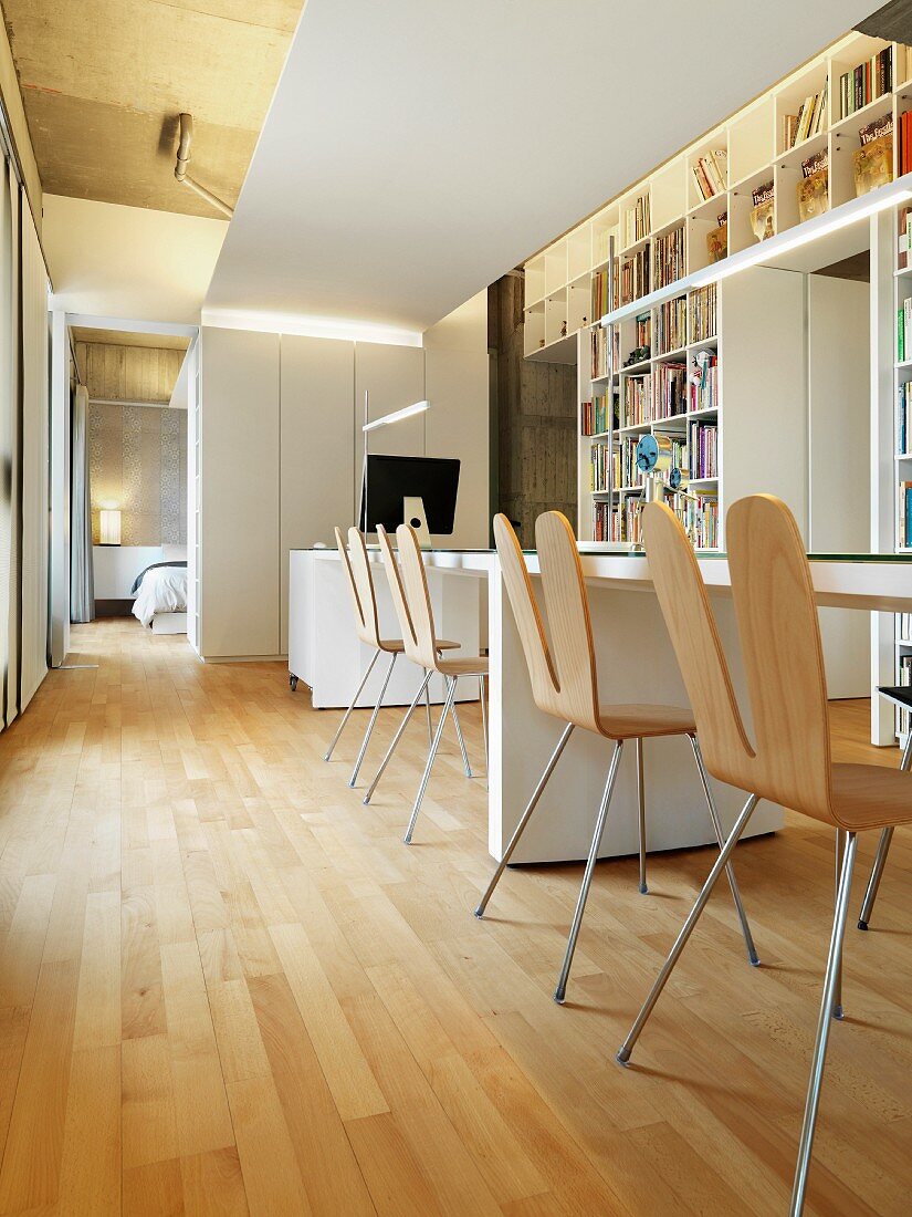 Designer Stühle an langem Tisch vor Einbauregalen und Schlafzimmer mit Doppelbett im Hintergrund