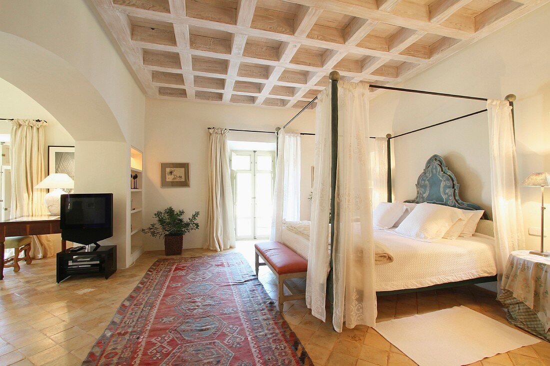 Himmelbett mit Vorhang unter Kassettendecke aus Holz in mediterranem Schlafzimmer