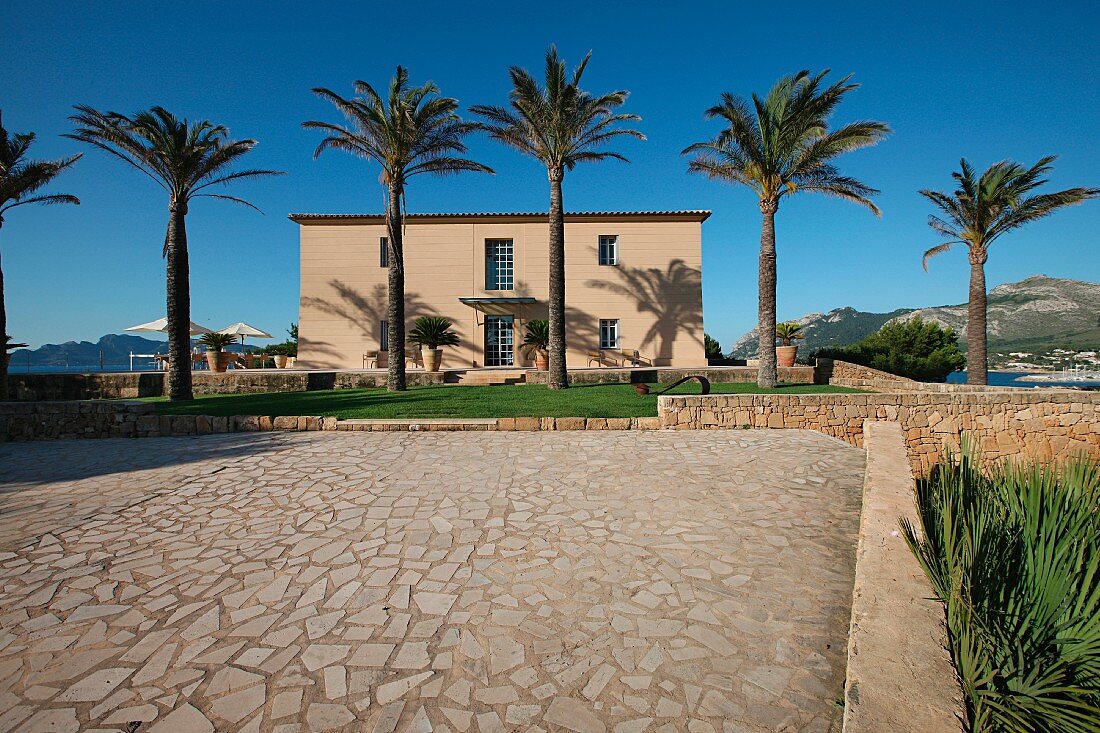 Offener Platz mit Natursteinboden und Palmenallee vor mediterranem Wohnhaus