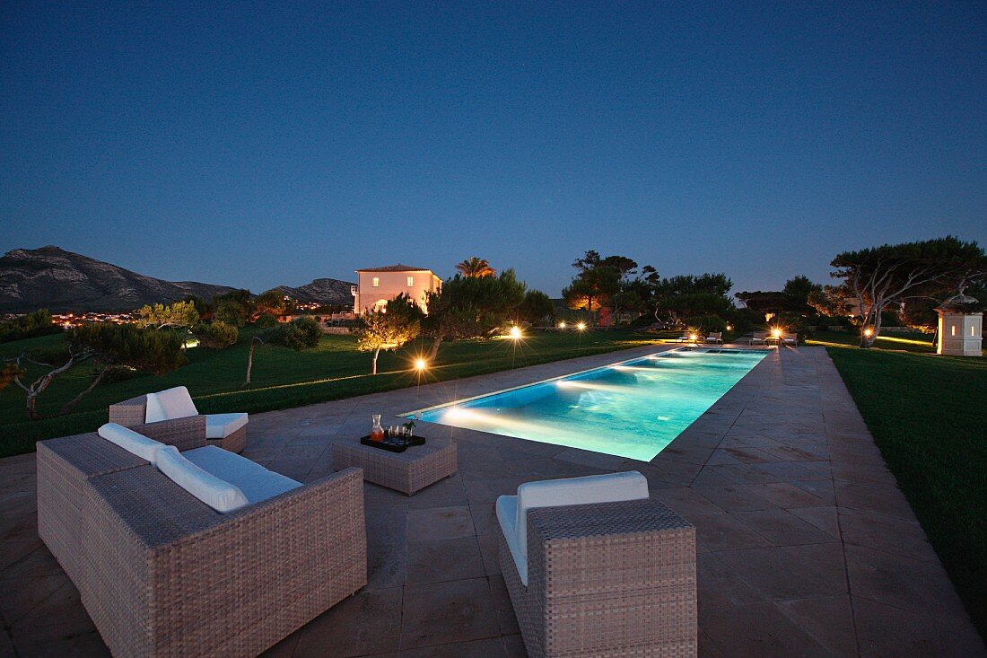 Beleuchteter Pool und elegante Outdoor Möbel auf Steinboden in Nachtstimmung